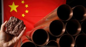 A person holds a piece of rare earth ore beside stacked metal tubes in front of China’s national flag, symbolizing China’s dominance in global mineral supply chains.