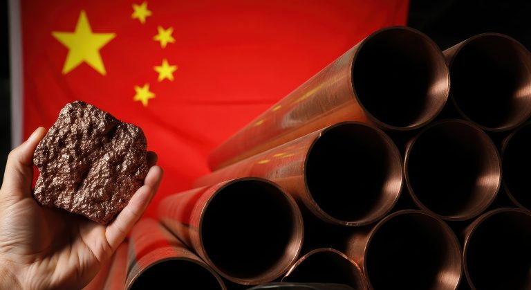 A person holds a piece of rare earth ore beside stacked metal tubes in front of China’s national flag, symbolizing China’s dominance in global mineral supply chains.
